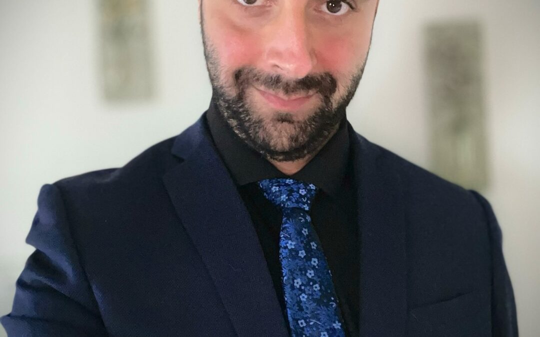 Portrait de Steven Atme portant un complet bleu marine et une cravate à motifs floraux bleus, souriant chaleureusement à la caméra. Il illustre son portrait intitulé « Le cœur du plaidoyer », une histoire axée sur la compassion, l’inclusion et la sensibilisation à la santé mentale.