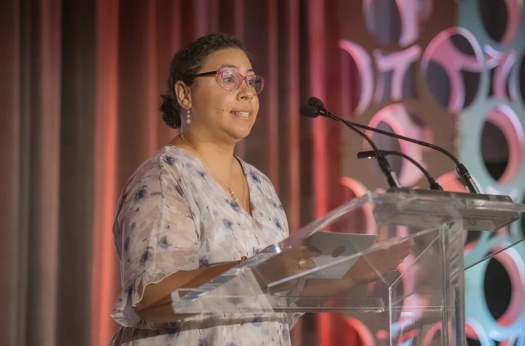 Photo de Sydney Elaine Butler debout à un pupitre transparent, prenant la parole avec passion lors d’un événement de remise de prix en ressources humaines, présentée dans leur histoire « Vivre avec passion ».